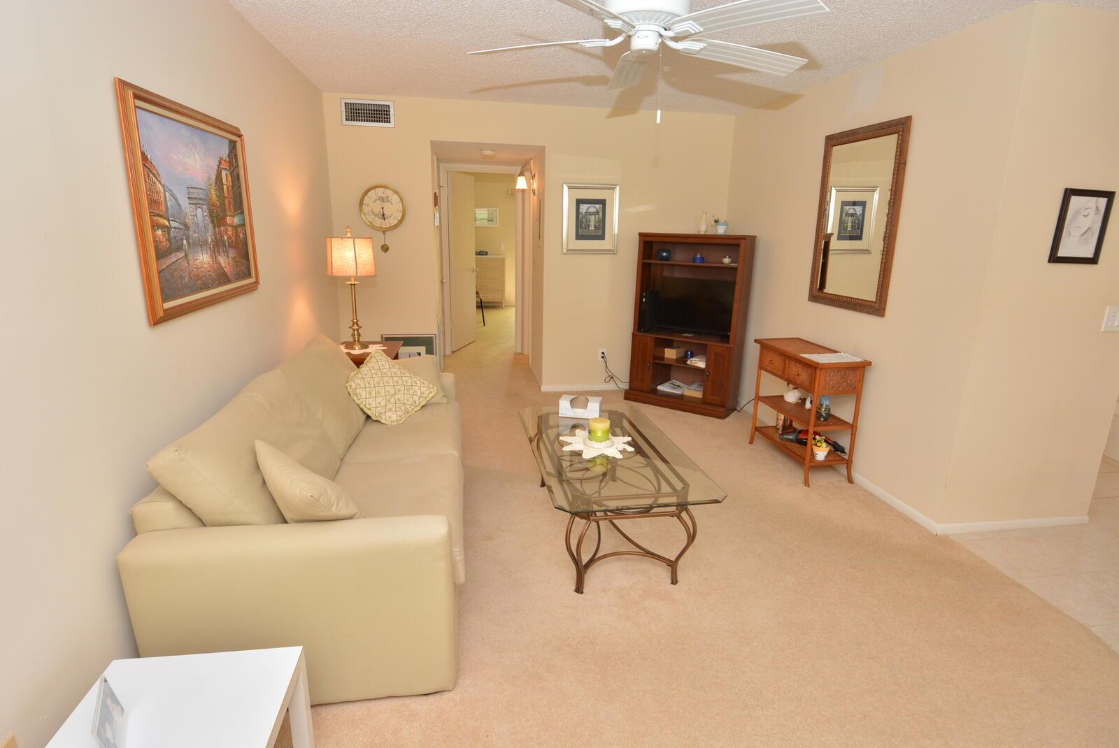 A living room with beige carpet, a tan sofa, a glass coffee table, and television console — 1225 NW 21st Street # 2105, Stuart FL 34994, STUART, FL