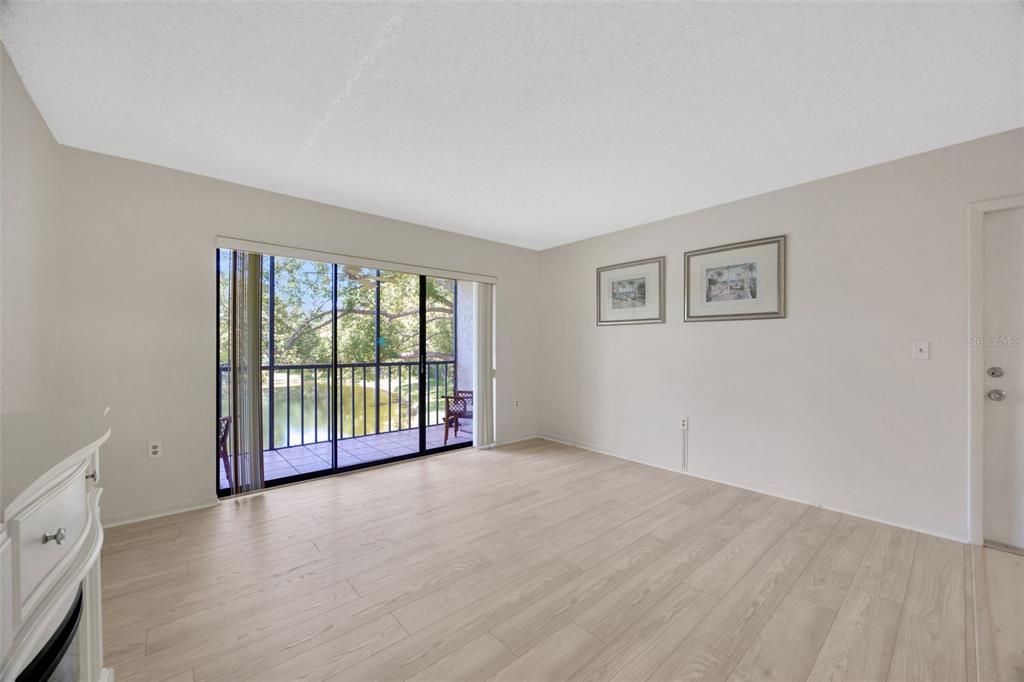 An empty room with light wood-look flooring, beige walls, and a sliding glass door to a balcony — 3134 LAKE PINE WAY UNIT F2, TARPON SPRINGS, FL