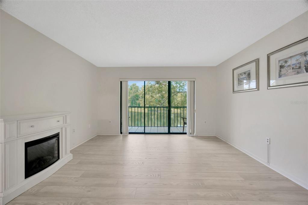 A living room with light wood-look flooring, a white fireplace, and a sliding glass door — 3134 LAKE PINE WAY UNIT F2, TARPON SPRINGS, FL
