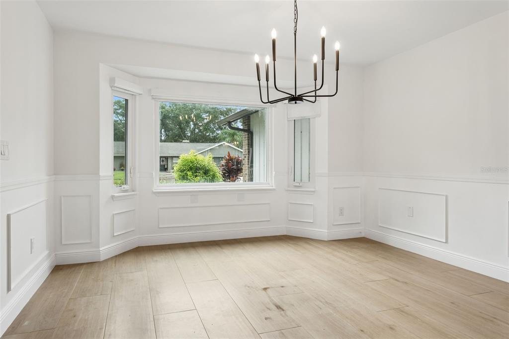 A dining room with light wood floors, white wainscoting, a bay window, and a black chandelier — 1046 SYLVIA LANE, TAMPA, FL