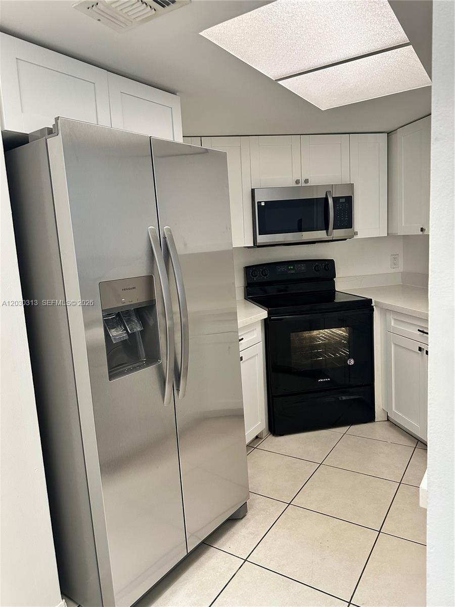 A kitchen features white cabinets, stainless steel appliances, a black stove, and light tile flooring — 9607 SW 138th Ave, Miami FL 33186, MIAMI, FL