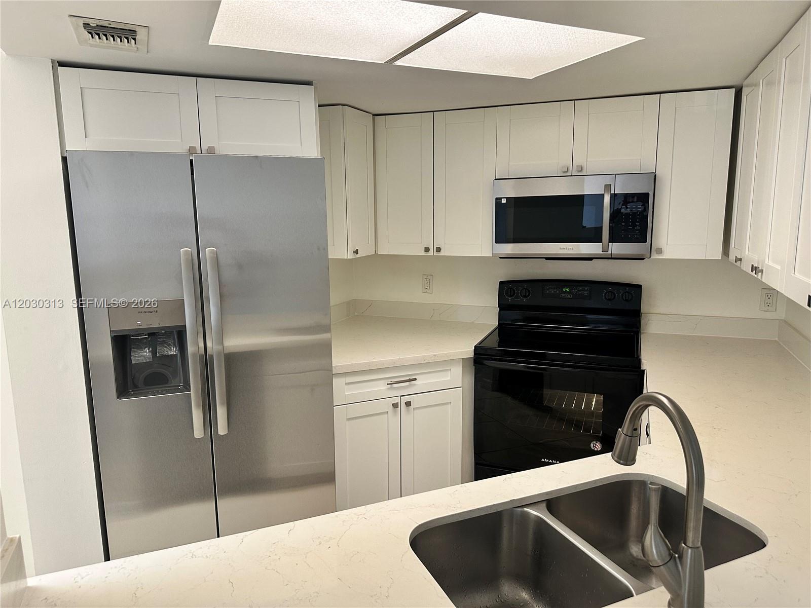 A kitchen features white cabinets, stainless steel appliances, a black stove, and light countertops — 9607 SW 138th Ave, Miami FL 33186, MIAMI, FL