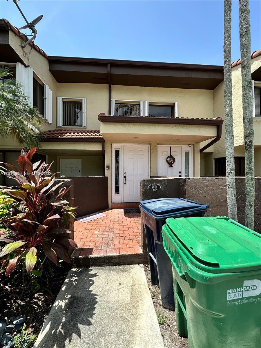 A two-story townhouse exterior features a brick walkway, white front doors, and two trash bins — 9607 SW 138th Ave, Miami FL 33186, MIAMI, FL