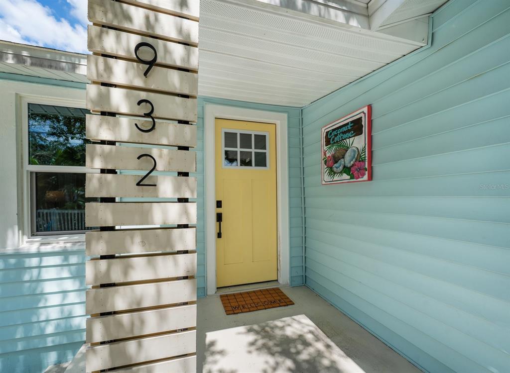 A yellow front door with a window sits on a porch with light blue siding — 932 HIGHLAND AVENUE, DUNEDIN, FL