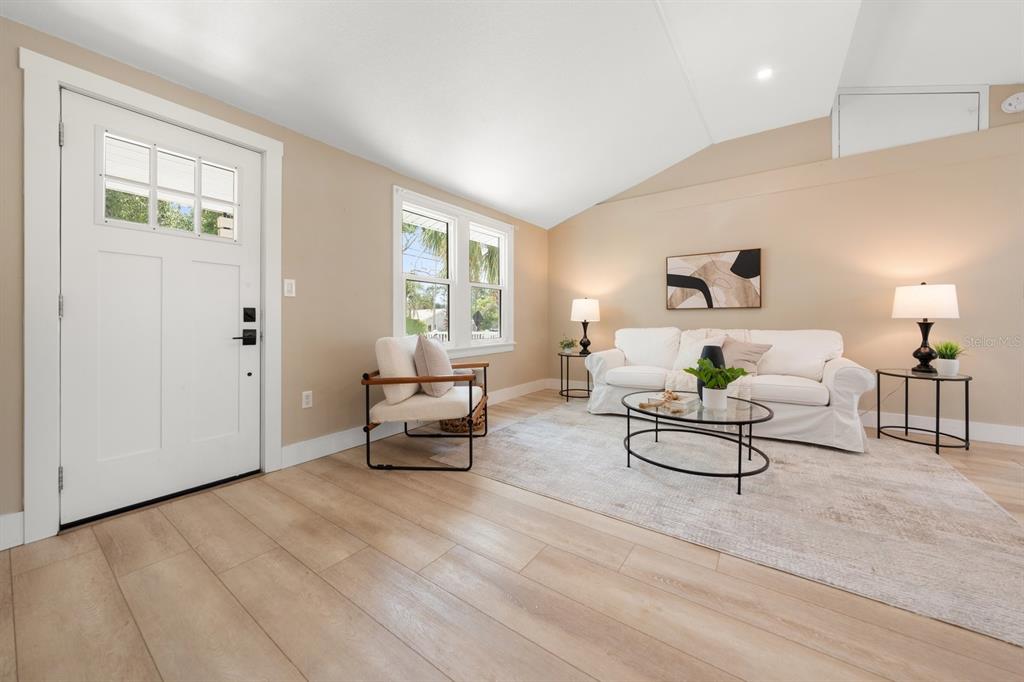 A living room features light wood flooring, a white sofa, an armchair, and a front door — 932 HIGHLAND AVENUE, DUNEDIN, FL