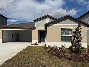 A single-story house exterior features a two-car garage, tan stucco walls, and a front entrance — 1629 TROPICAL OASIS AVENUE, PLANT CITY, FL