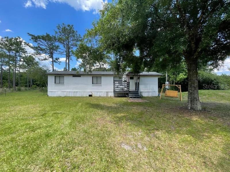 A single-story mobile home with white siding sits on a grassy lot with trees — 9285 LUNA DRIVE, ST CLOUD, FL