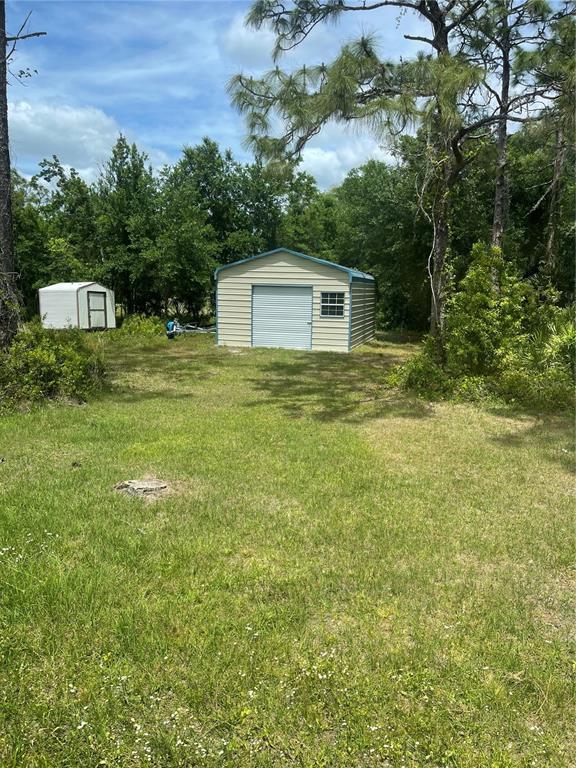 A grassy yard features a metal storage shed and a smaller white shed near trees — 9285 LUNA DRIVE, ST CLOUD, FL