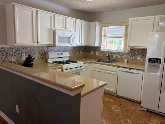 A kitchen features white cabinets, a patterned tile backsplash, tan countertops, and white appliances — 17663 SE 92ND GRANTHAM TERRACE, THE VILLAGES, FL