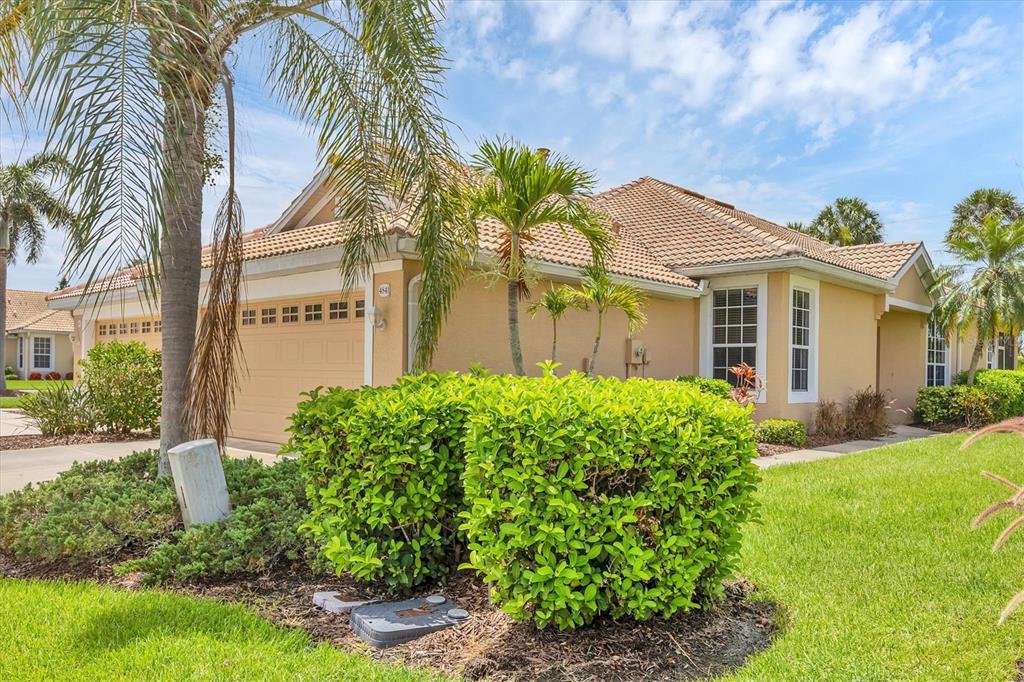 A tan single-story house with a tile roof, a two-car garage, and manicured landscaping — 4841 WHISPERING OAKS DRIVE, NORTH PORT, FL