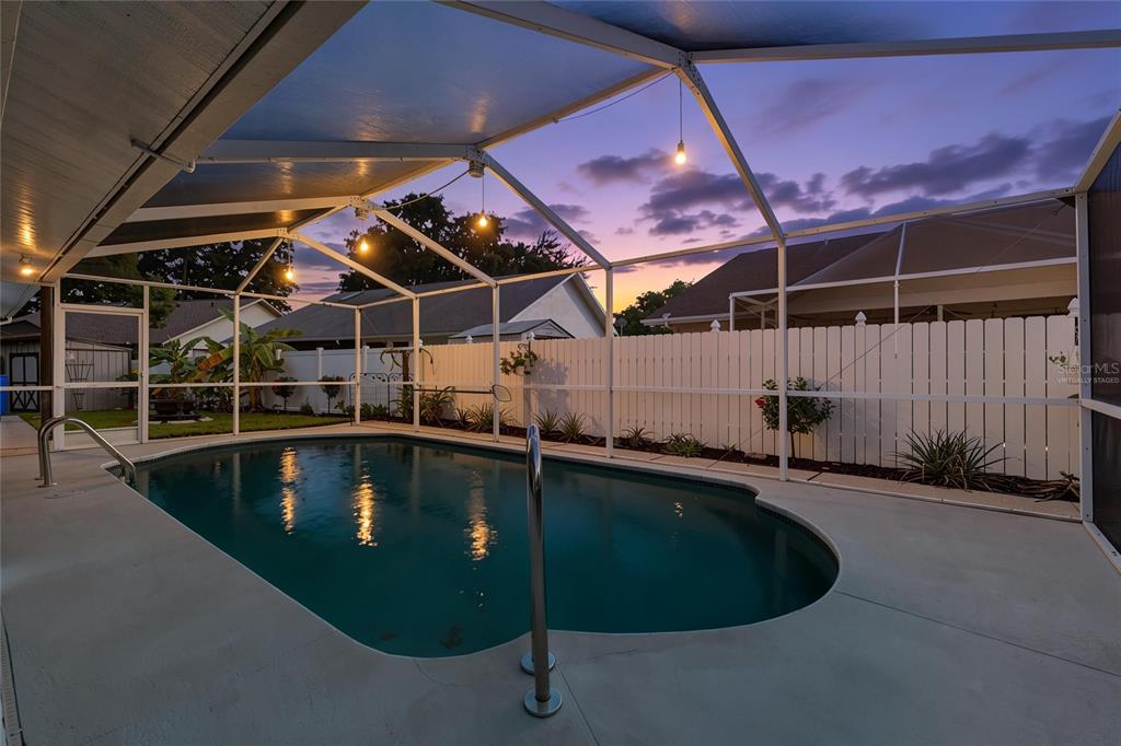 A screened-in swimming pool with a concrete deck sits in a backyard at sunset — 4607 SAWGRASS BOULEVARD, NEW PORT RICHEY, FL