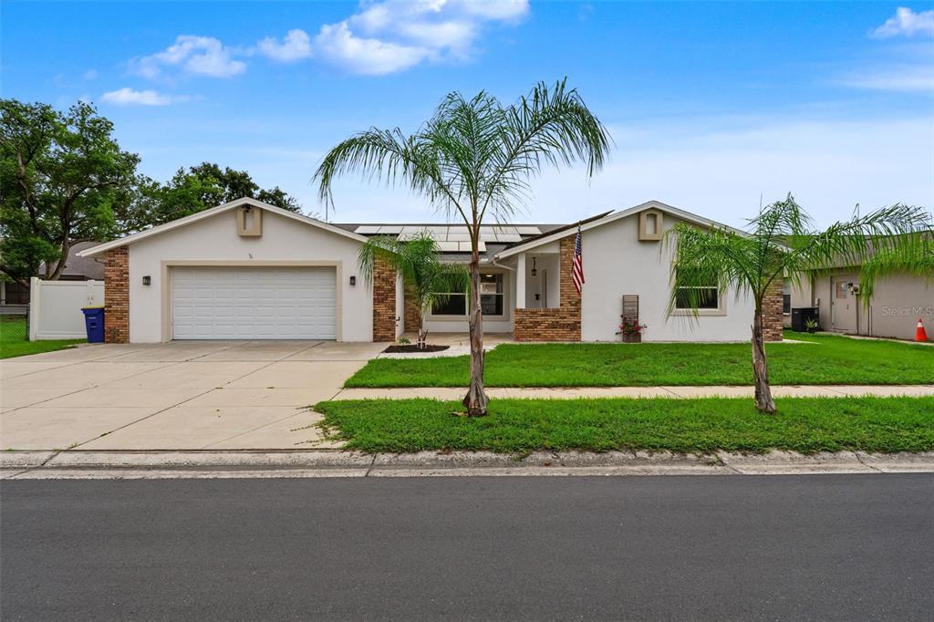 A single-story house with a white stucco facade, brick accents, a two-car garage, and palm trees — 4607 SAWGRASS BOULEVARD, NEW PORT RICHEY, FL