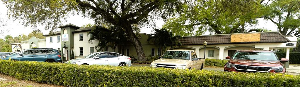 A low-rise commercial building with a hedge in the foreground and parked cars — 2001 MANATEE AVENUE E UNIT 104, BRADENTON, FL