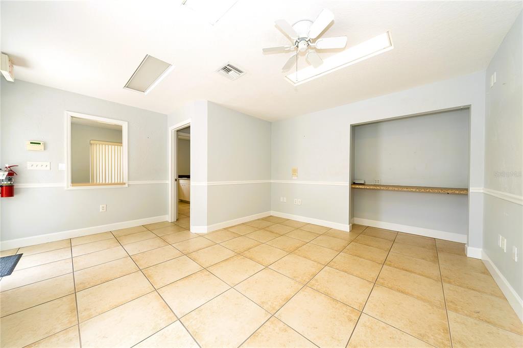 An empty room with light blue walls, tan tile flooring, a ceiling fan, and built-in shelving — 2001 MANATEE AVENUE E UNIT 104, BRADENTON, FL