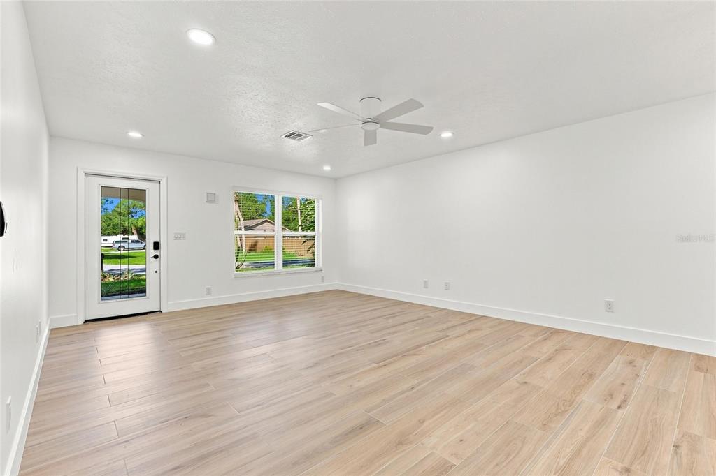 An empty room features light wood-look flooring, white walls, a ceiling fan, and a glass-paneled door — 2881 POPPY ROAD, VENICE, FL