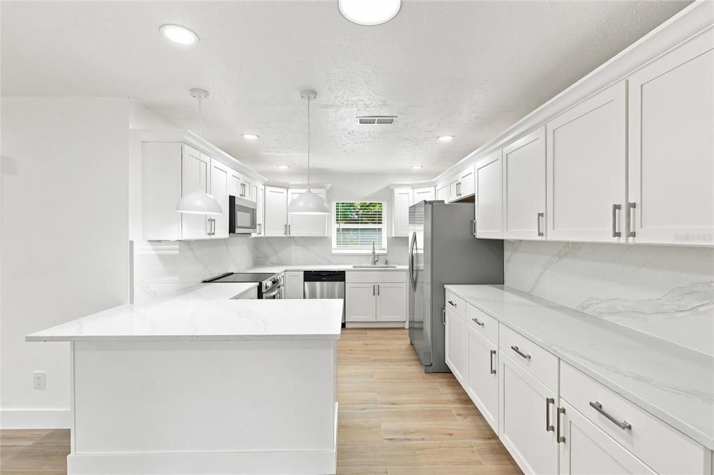 A bright kitchen features white cabinets, marble-look countertops, stainless steel appliances, and light wood flooring — 2881 POPPY ROAD, VENICE, FL