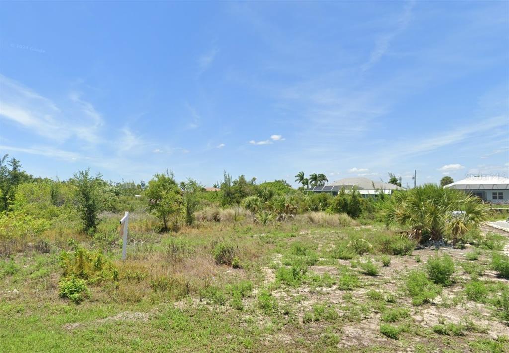 A vacant, overgrown lot with scattered shrubs and trees under a bright blue sky — 15642 APPLEWHITE CIRCLE, PORT CHARLOTTE, FL