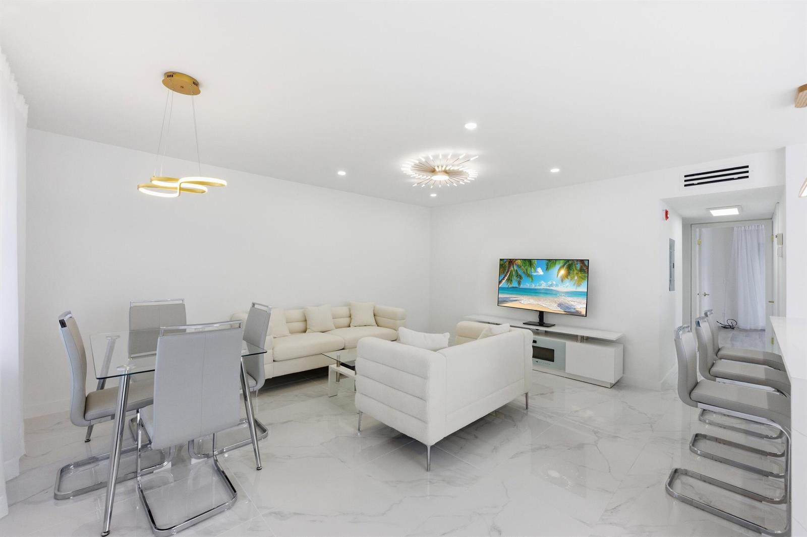 A modern, all-white living and dining area features marble-look tile floors and contemporary furniture — 618 Normandy M, Delray Beach FL 33484, DELRAY BEACH, FL
