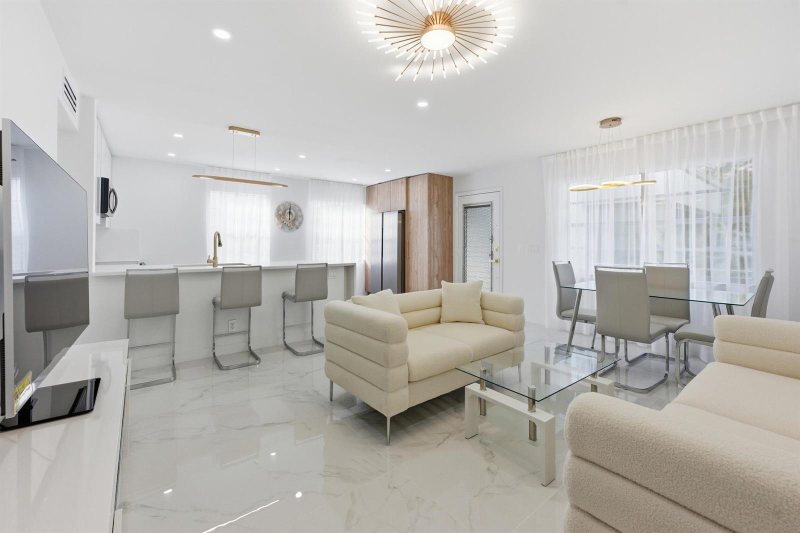 A modern open-concept living room and kitchen featuring white marble floors and cream-colored sofas — 618 Normandy M, Delray Beach FL 33484, DELRAY BEACH, FL