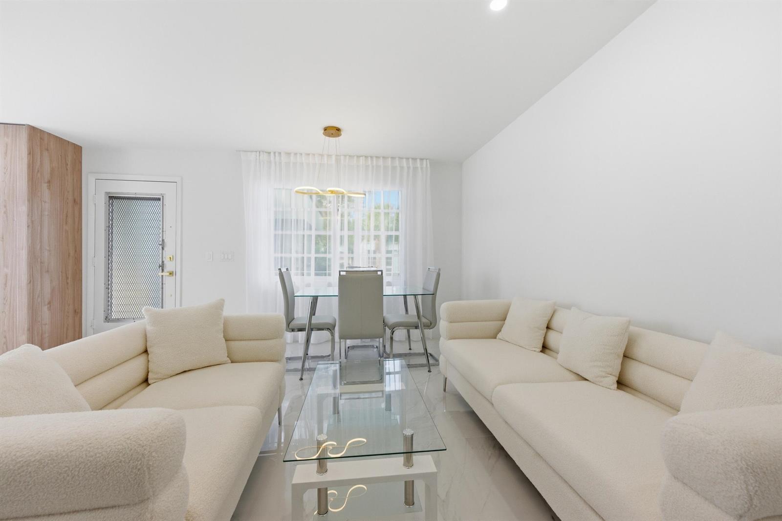 A bright living and dining area features white sofas, a glass coffee table, and tile flooring — 618 Normandy M, Delray Beach FL 33484, DELRAY BEACH, FL