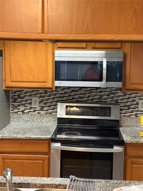 A kitchen features wood cabinets, a stainless steel microwave, a glass-top stove, and mosaic backsplash — 2717 N POINCIANA BOULEVARD UNIT 169, KISSIMMEE, FL