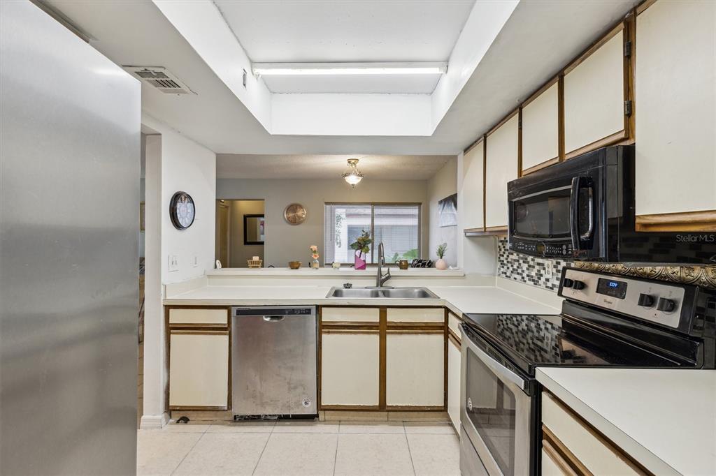A kitchen with white cabinets, stainless steel appliances, and a pass-through window to the dining area — 2554 LAKEWAY BRANCH DRIVE UNIT 3001, ORLANDO, FL