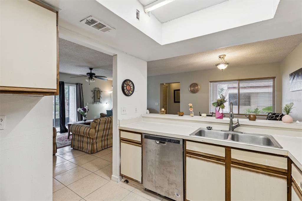 A kitchen with a stainless steel dishwasher and sink overlooks a living area with tile — 2554 LAKEWAY BRANCH DRIVE UNIT 3001, ORLANDO, FL