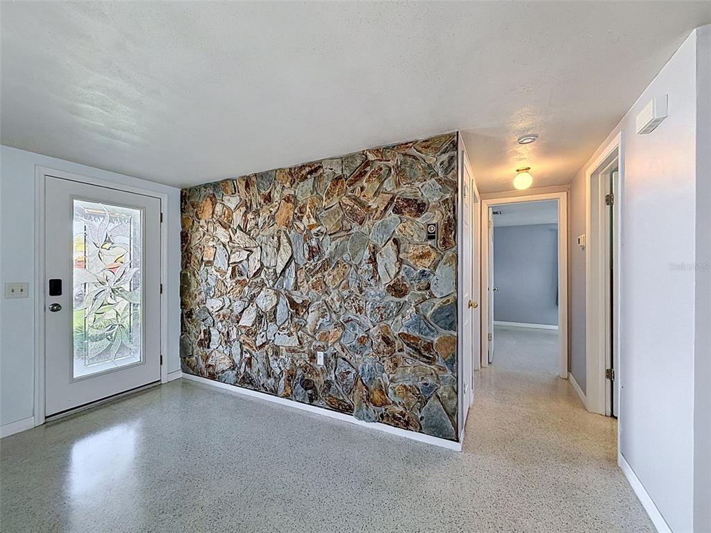 An entryway features a stone accent wall, a glass-paneled door, and light-colored speckled flooring — 12800 5TH ISLE, HUDSON, FL
