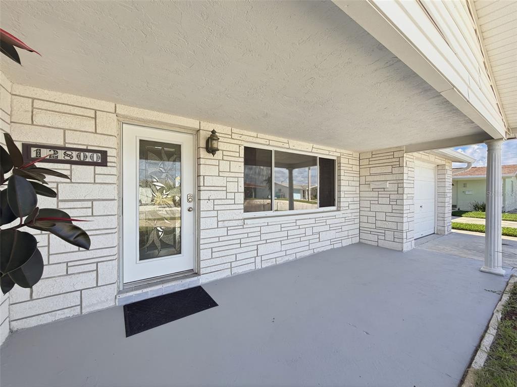 A covered porch features a white stone facade, a glass-paneled front door, and a gray floor — 12800 5TH ISLE, HUDSON, FL