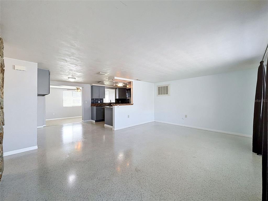 An open-concept living area features light-colored terrazzo flooring, white walls, and a pass-through kitchen — 12800 5TH ISLE, HUDSON, FL