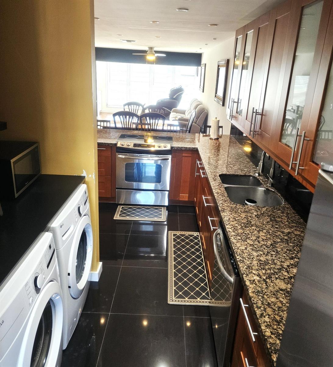A galley kitchen features dark wood cabinets, granite countertops, stainless steel appliances, and black tile — 1141 Violet Terrace # 201, Delray Beach FL 33445, DELRAY BEACH, FL