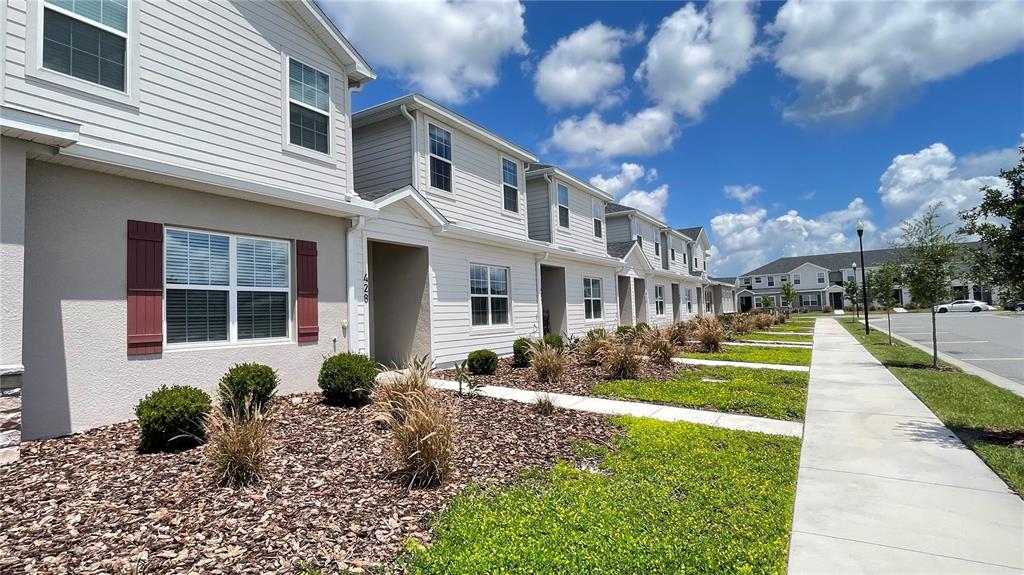 A row of light-colored townhouses features red shutters, brown mulch landscaping, and a concrete sidewalk — 428 HUCKLEBERRY DRIVE, ST CLOUD, FL