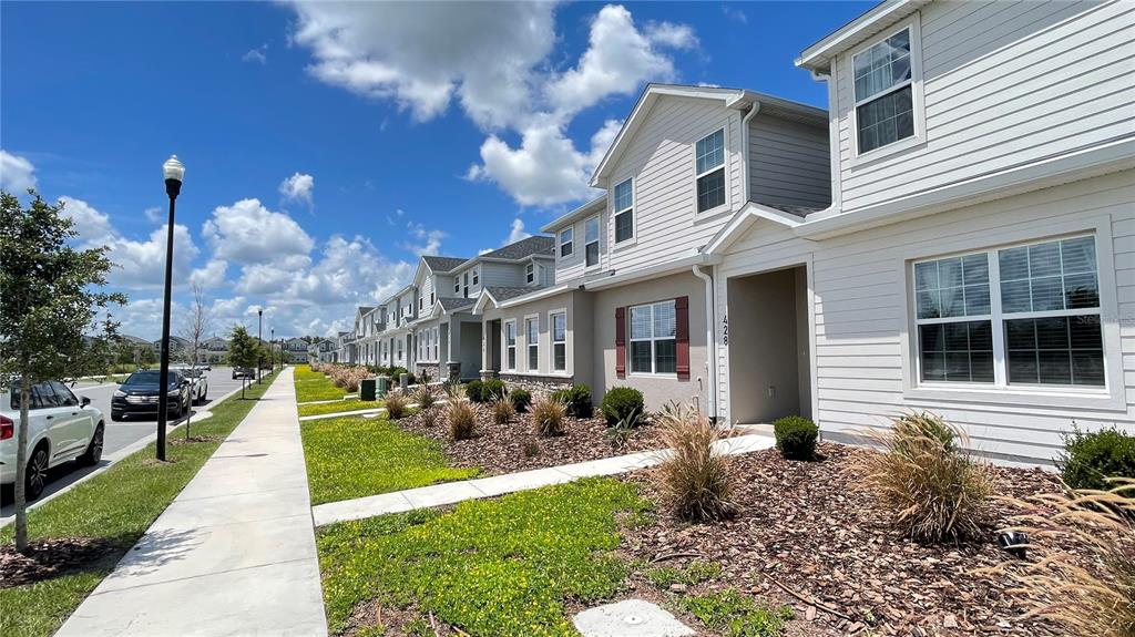A row of two-story townhomes with light siding and a sidewalk under a blue sky — 428 HUCKLEBERRY DRIVE, ST CLOUD, FL