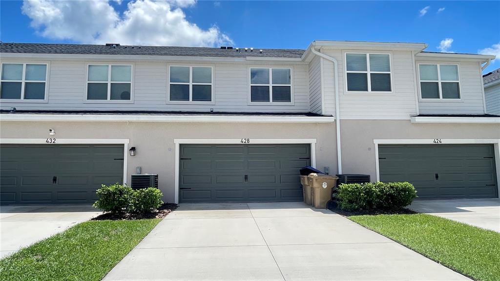 A row of three townhouses features gray garage doors, light siding, and concrete driveways — 428 HUCKLEBERRY DRIVE, ST CLOUD, FL