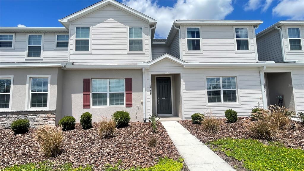 A two-story townhouse exterior features light siding, a dark front door, and landscaped mulch beds — 428 HUCKLEBERRY DRIVE, ST CLOUD, FL