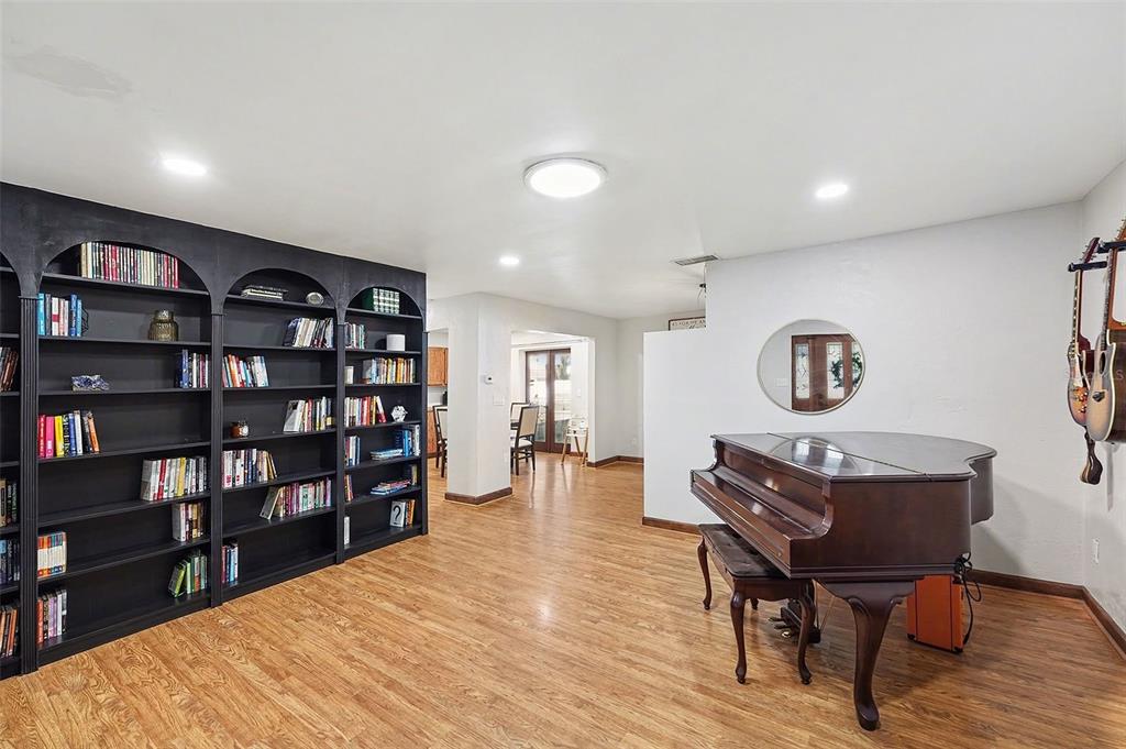 A room with wood-look flooring, a large black bookshelf, and a grand piano — 5967 102ND AVENUE N, PINELLAS PARK, FL