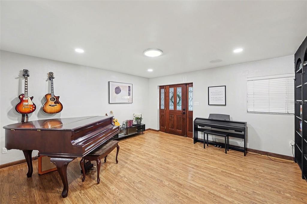 A music room features a grand piano, two guitars on the wall, and wood-look flooring — 5967 102ND AVENUE N, PINELLAS PARK, FL