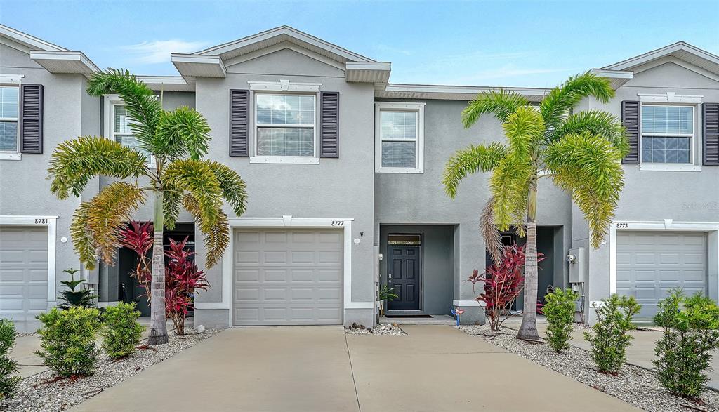 The exterior of a multi-unit townhouse features gray stucco walls, garage doors, and palm trees — 8777 MILESTONE DRIVE, SARASOTA, FL