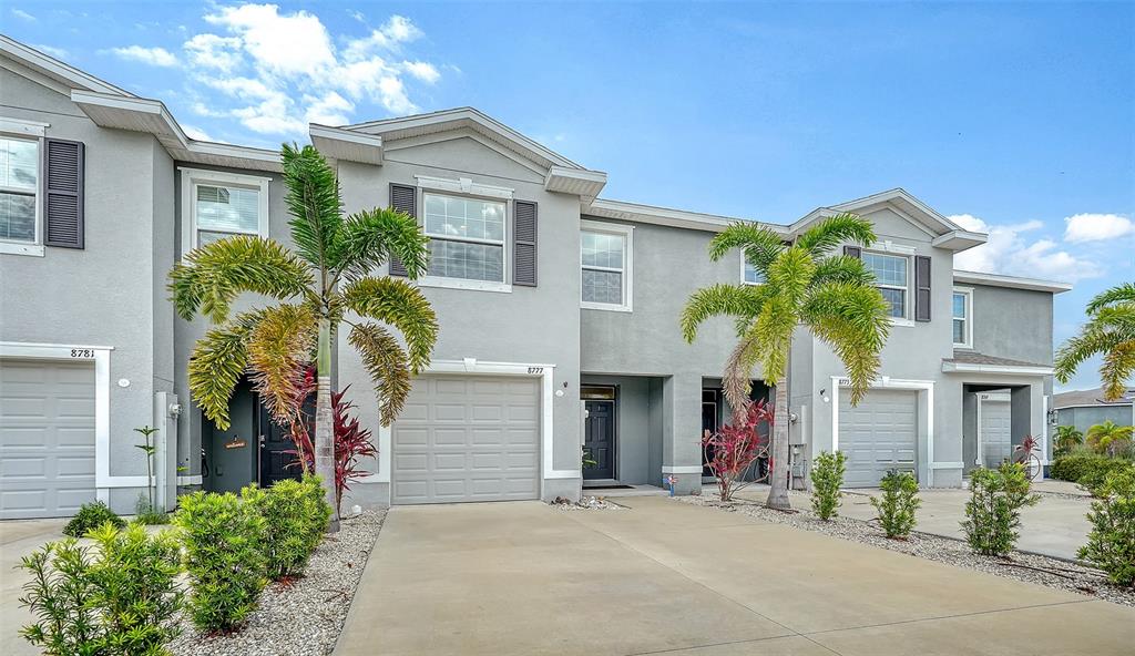 A row of light gray townhouses features attached garages, palm trees, and concrete driveways — 8777 MILESTONE DRIVE, SARASOTA, FL