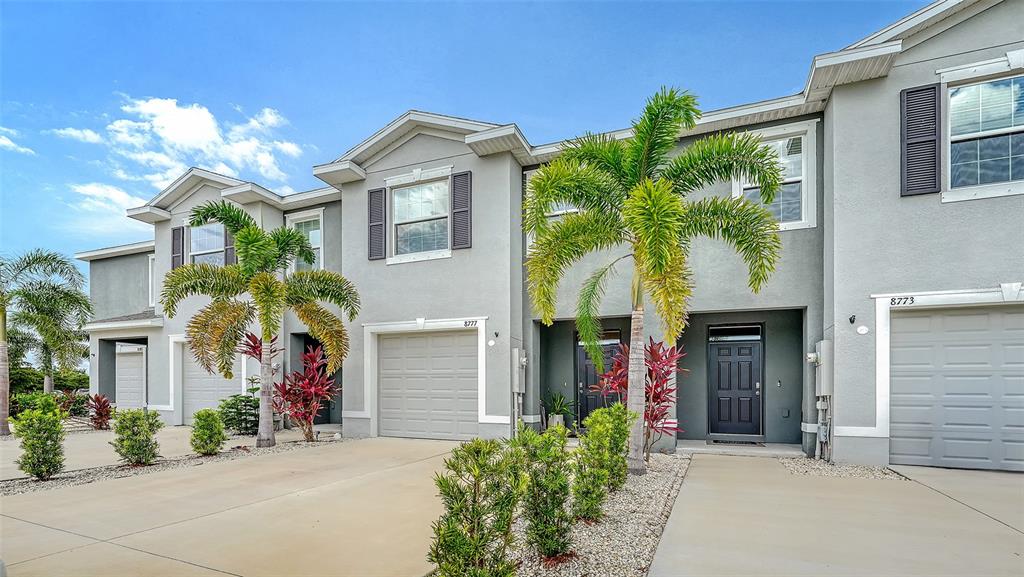 A row of two-story townhouses with gray stucco exteriors, attached garages, and palm trees — 8777 MILESTONE DRIVE, SARASOTA, FL