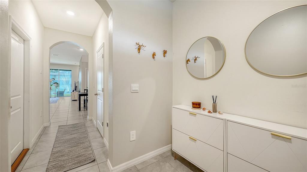 A bright entryway features white shoe cabinets, round mirrors, and a tiled hallway leading indoors — 8777 MILESTONE DRIVE, SARASOTA, FL