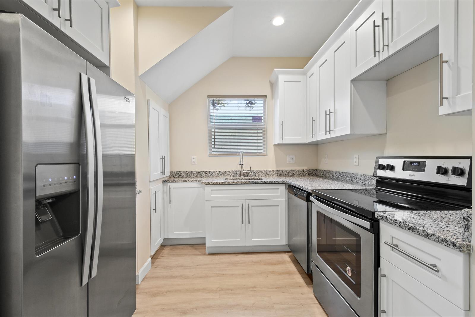 A kitchen features white cabinets, granite countertops, stainless steel appliances, and light wood-look flooring — 627 Bunker Road, West Palm Beach FL 33405, WEST PALM BEACH, FL
