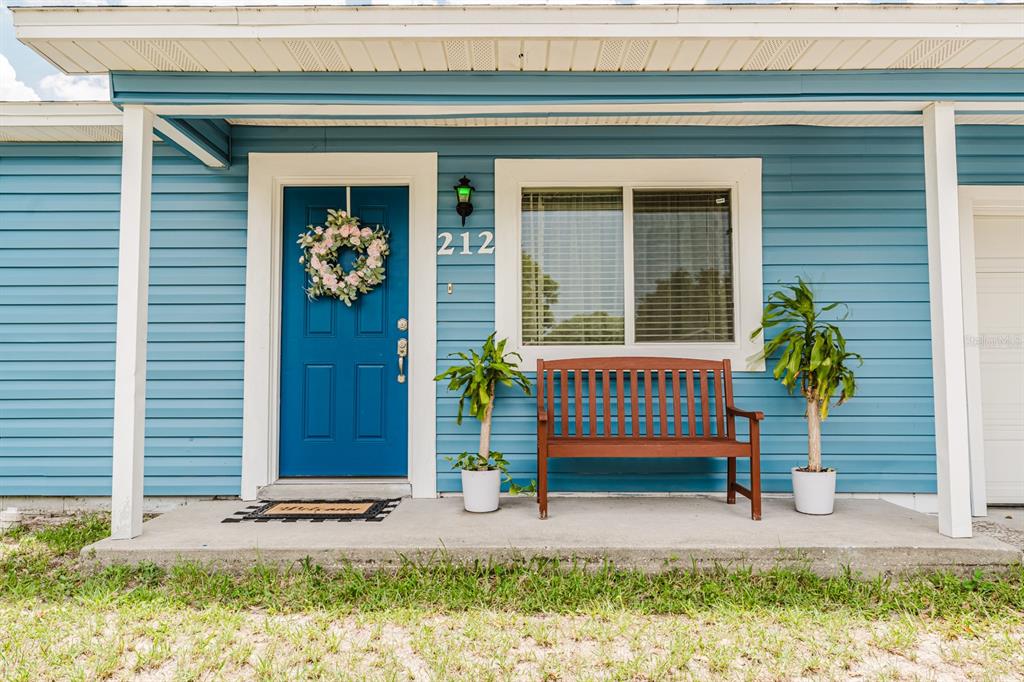 A blue-sided house exterior features a front door with a wreath, a bench, and plants — 212 SUMMERSET DRIVE, APOPKA, FL
