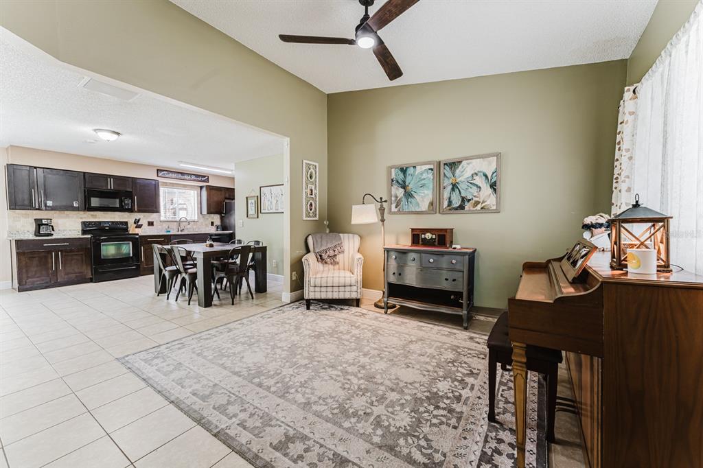 A living area with a piano and armchair flows into an open-concept kitchen and dining space — 212 SUMMERSET DRIVE, APOPKA, FL