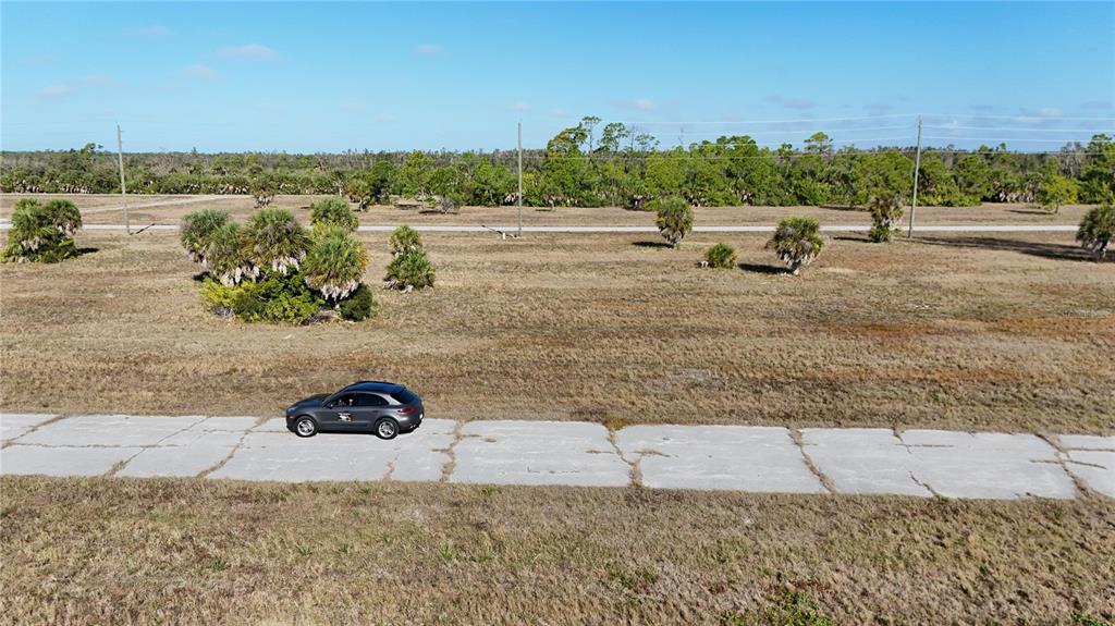 A dark SUV is parked on a cracked concrete road in a large, grassy field — 14381 SWORDFISH COURT, PLACIDA, FL