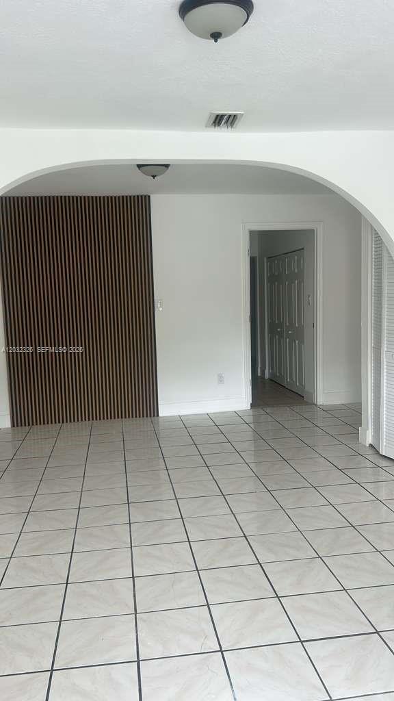An interior room features white tile flooring, an arched doorway, and a wood-slat accent wall — 2467 NW 103rd St, Miami FL 33147, MIAMI, FL