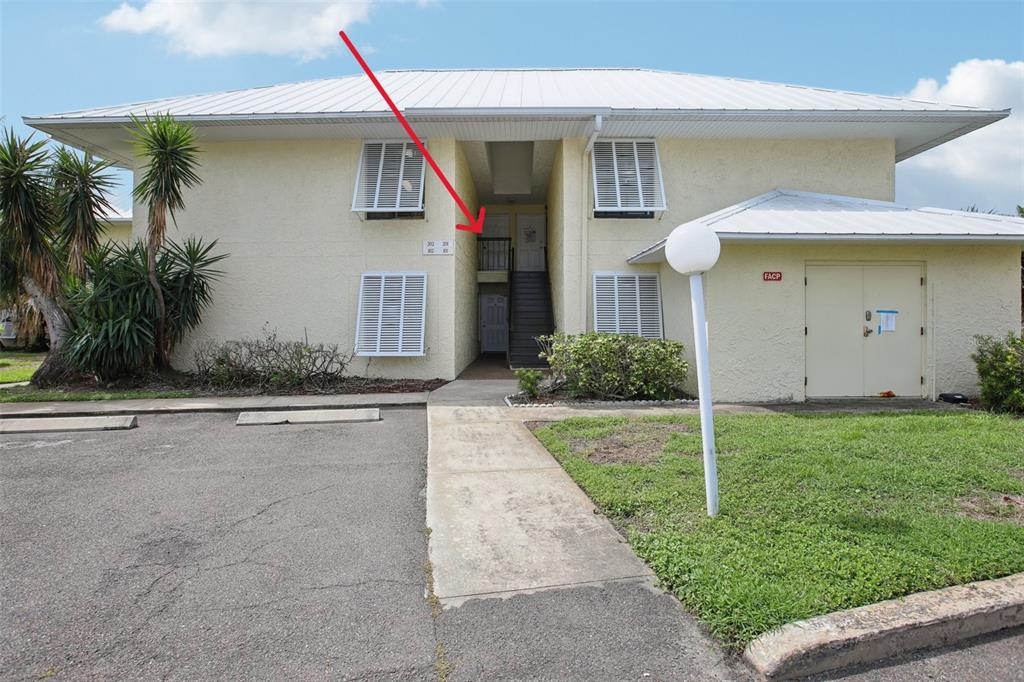The exterior of a two-story apartment building features a central staircase and a red arrow — 7300 SUNSHINE SKYWAY LANE S UNIT 202, ST PETERSBURG, FL