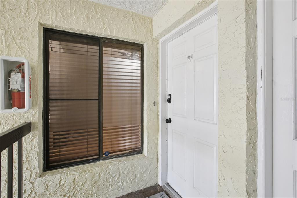 An exterior view of an apartment entrance with a white door, window, and fire extinguisher — 7300 SUNSHINE SKYWAY LANE S UNIT 202, ST PETERSBURG, FL