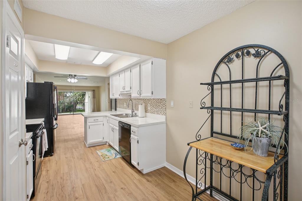 A kitchen with white cabinets, black appliances, light wood flooring, and a decorative metal rack — 7300 SUNSHINE SKYWAY LANE S UNIT 202, ST PETERSBURG, FL
