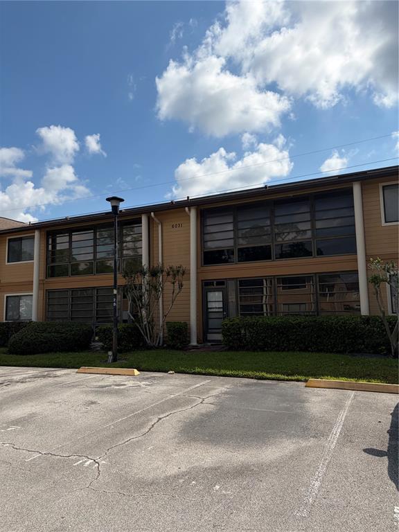 A two-story apartment building with tan siding and large windows sits behind a parking lot — 6031 SCOTCHWOOD GLEN UNIT 205, ORLANDO, FL